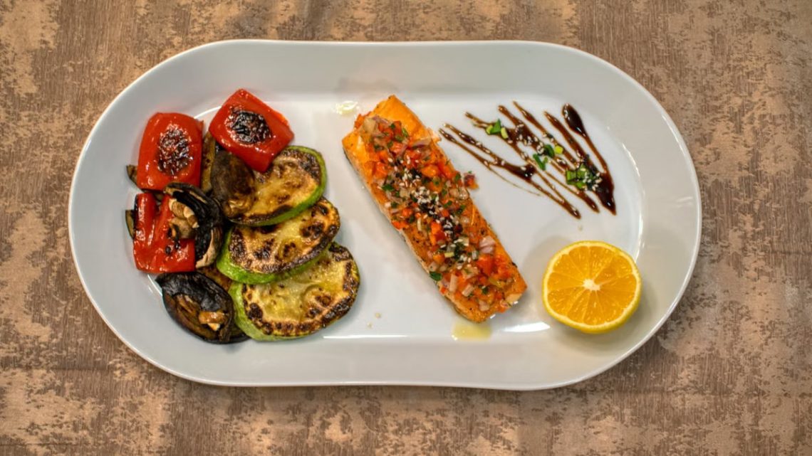 Gourmet grilled salmon served with roasted vegetables and lemon slice on a white plate.
