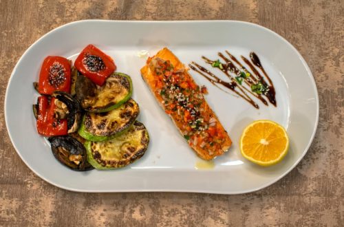 Gourmet grilled salmon served with roasted vegetables and lemon slice on a white plate.