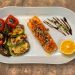 Gourmet grilled salmon served with roasted vegetables and lemon slice on a white plate.