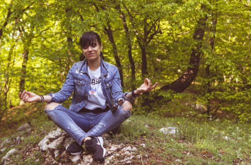 A woman meditates peacefully in a lush green forest, exuding calm and relaxation.