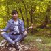 A woman meditates peacefully in a lush green forest, exuding calm and relaxation.